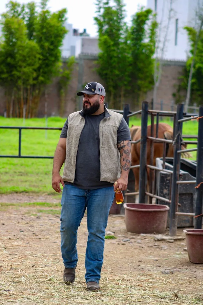 Beige Fleece Vest, Charcoal T-Shirt, Blue Jeans, and Graphic Baseball Cap