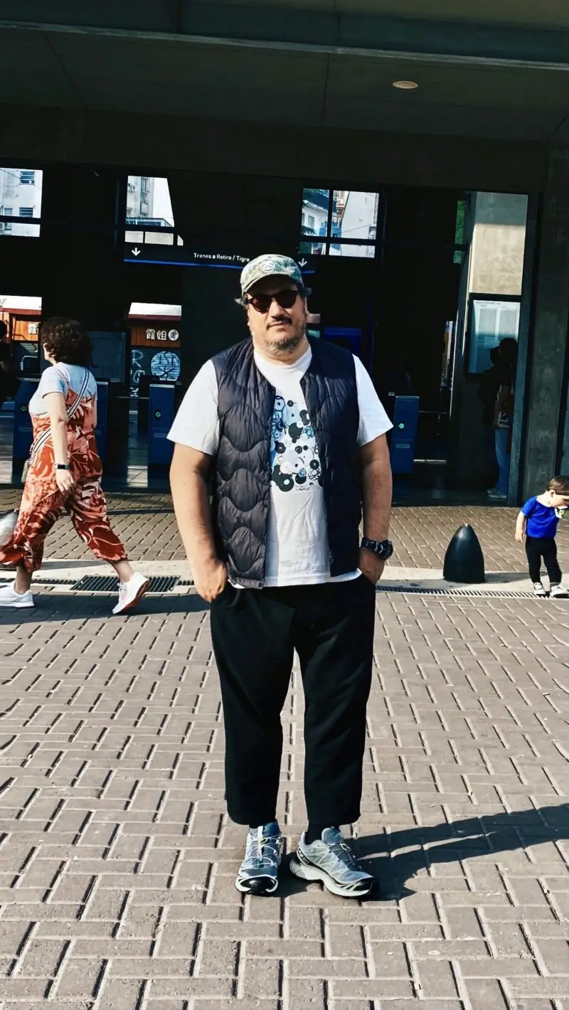 Black Quilted Vest, White Graphic T-Shirt, Black Pants, and Camo Baseball Cap