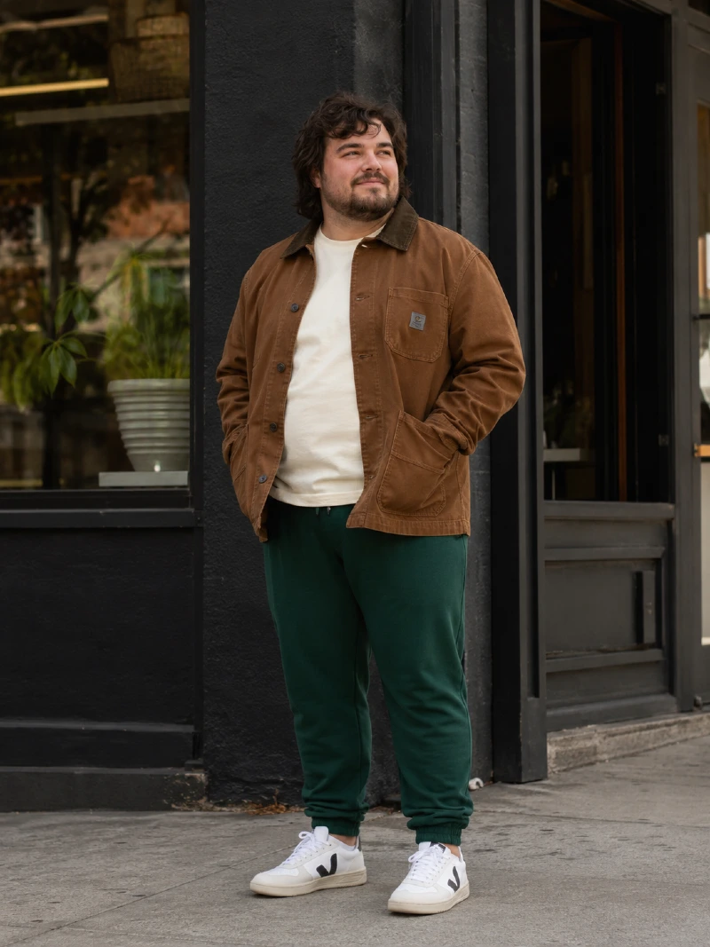 Brown Canvas Work Jacket, Off-White T-Shirt, Dark Green Sweatpants, and White Sneakers