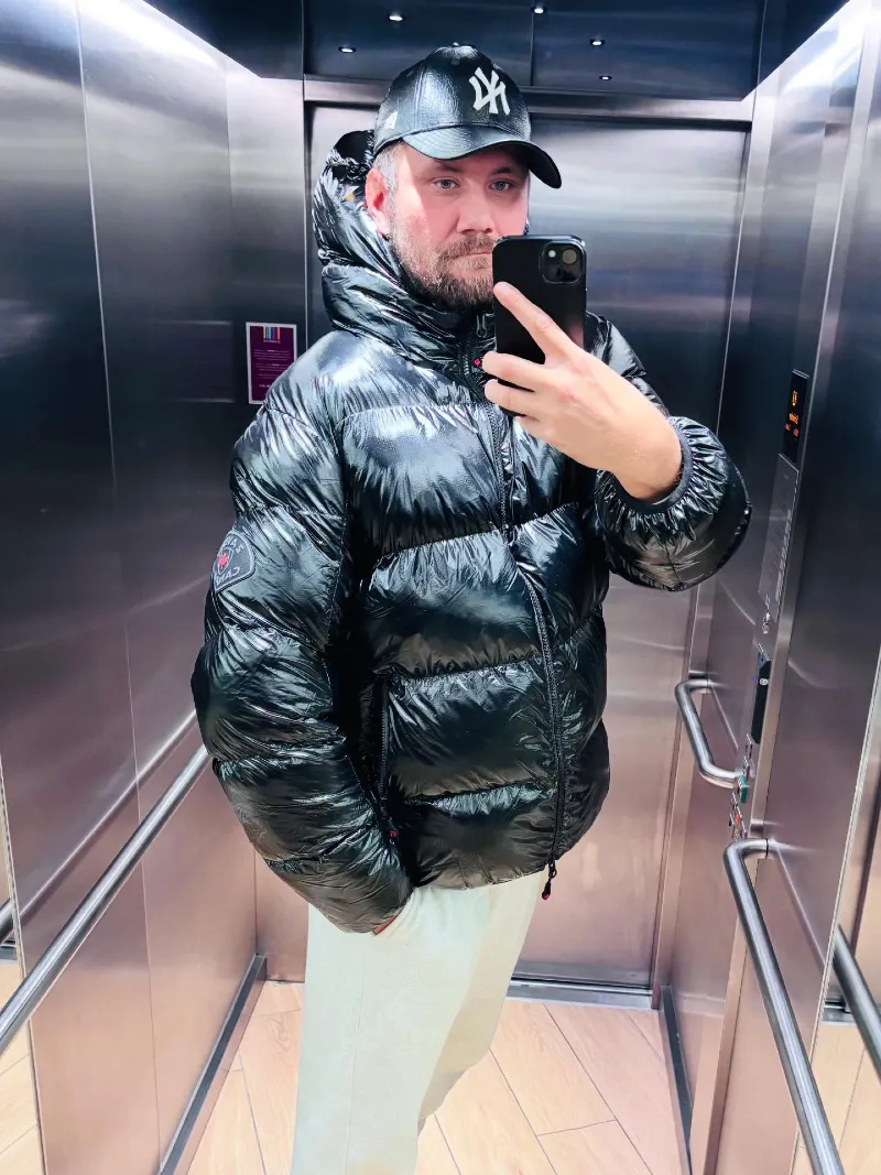 Shiny Black Hooded Puffer Jacket with White Sweatpants and Baseball Cap