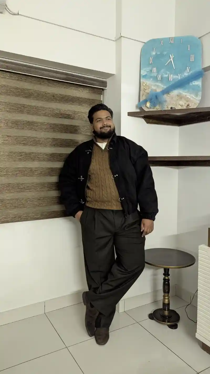 black jacket, brown cable knit sweater, dark trousers, and suede shoes