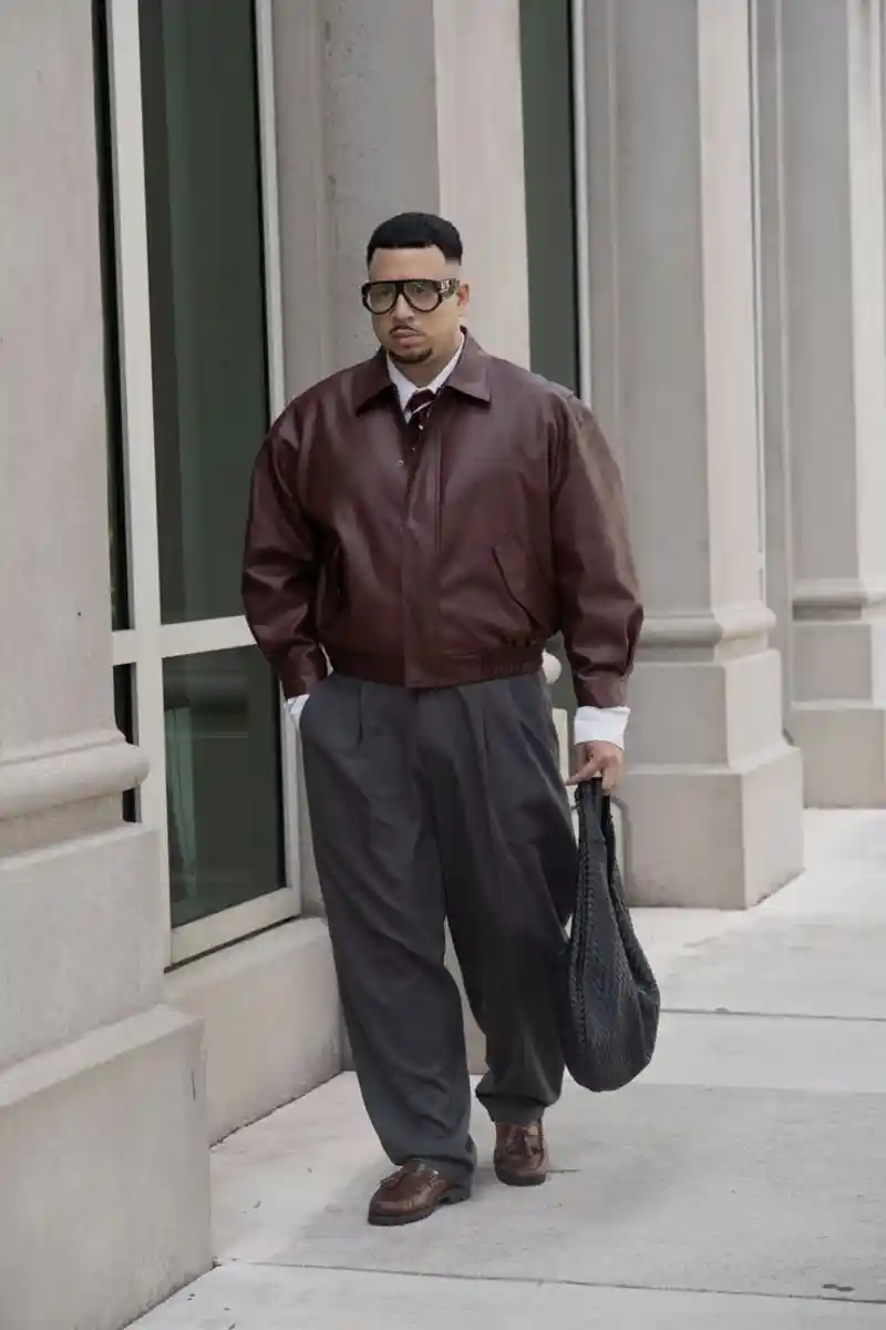 brown leather bomber jacket, white button-up shirt, tie, dark grey pleated trousers, and brown tassel loafers